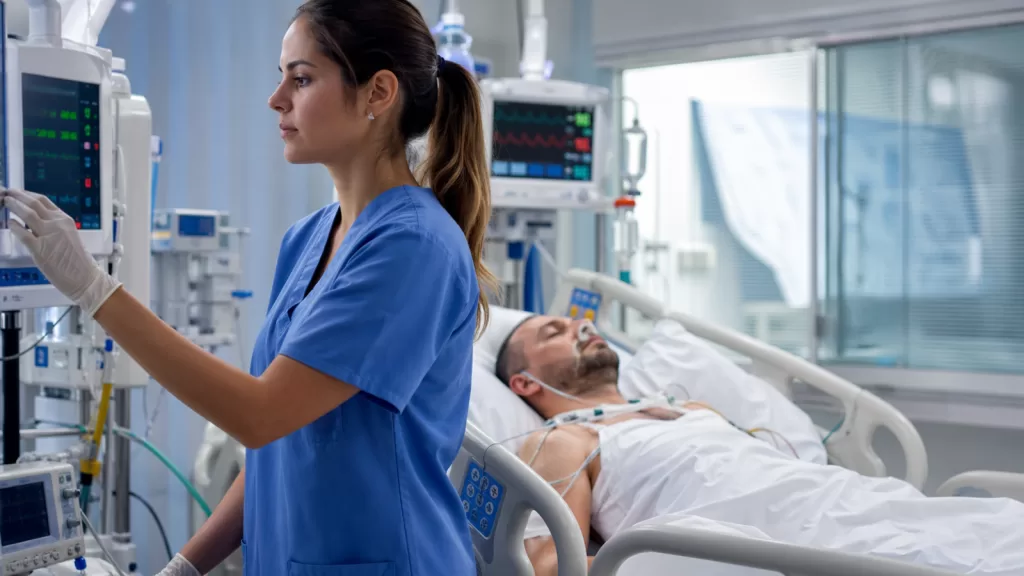 Técnica de enfermagem monitorando paciente em leito de UTI com equipamentos hospitalares ao redor