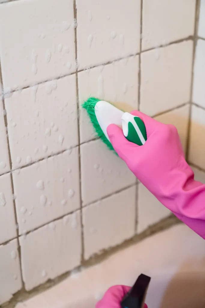 Primer plano de una mano con guante usando un cepillo pequeño sobre las juntas de azulejos del baño
