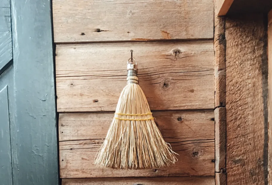 Escoba y recogedor colgados en una pared de madera en una zona de limpieza ordenada y seca